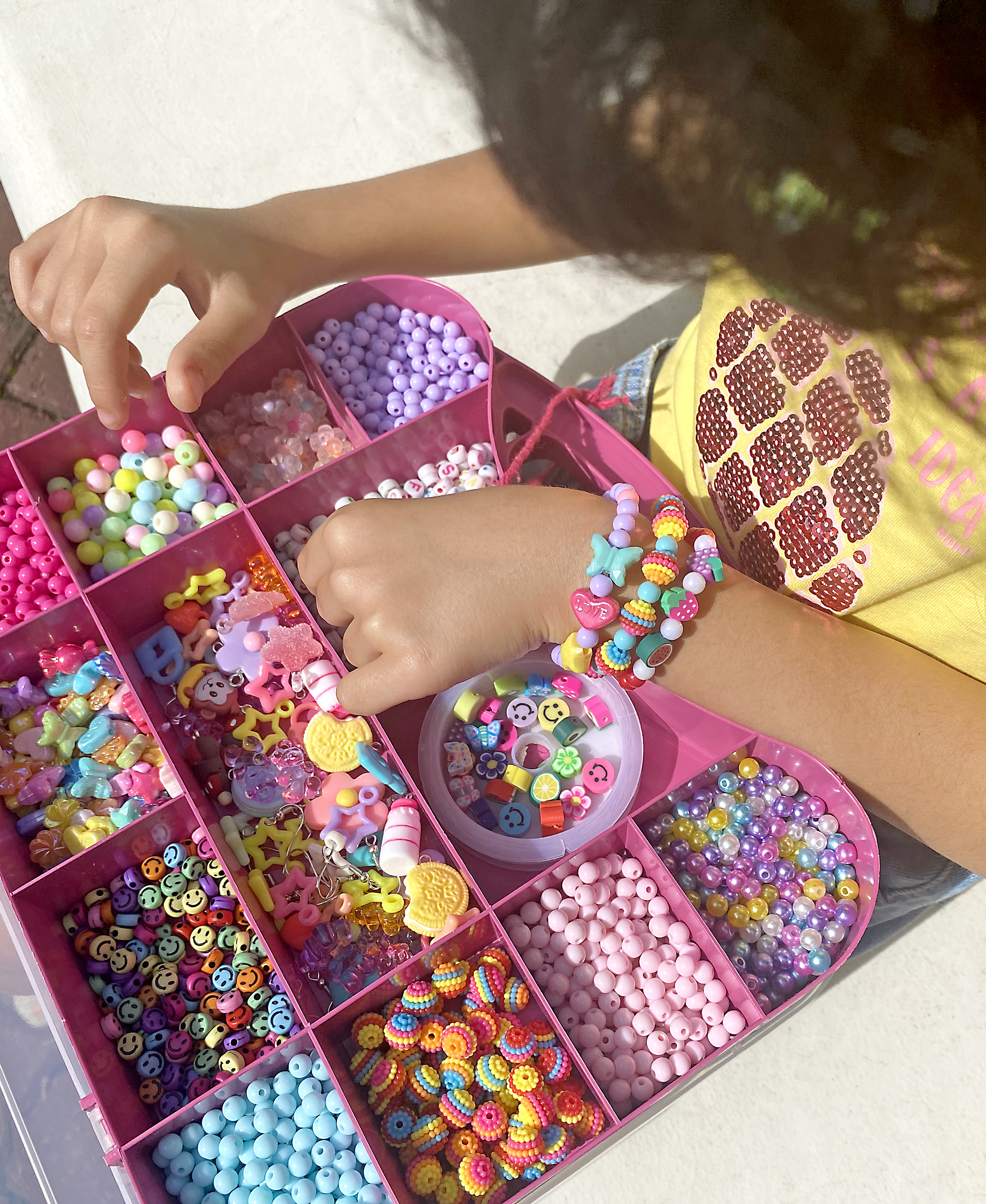 Criança montando pulseiras com miçangas coloridas em maleta rosa